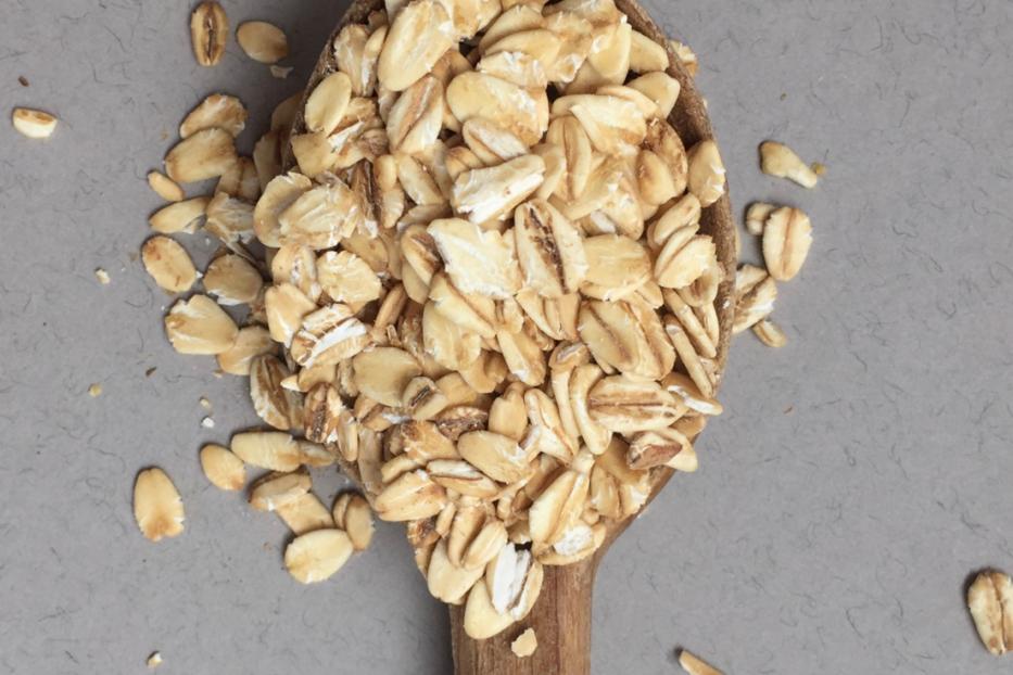 Ein Holzlöffel voller Haferflocken auf einem grauen Untergrund.