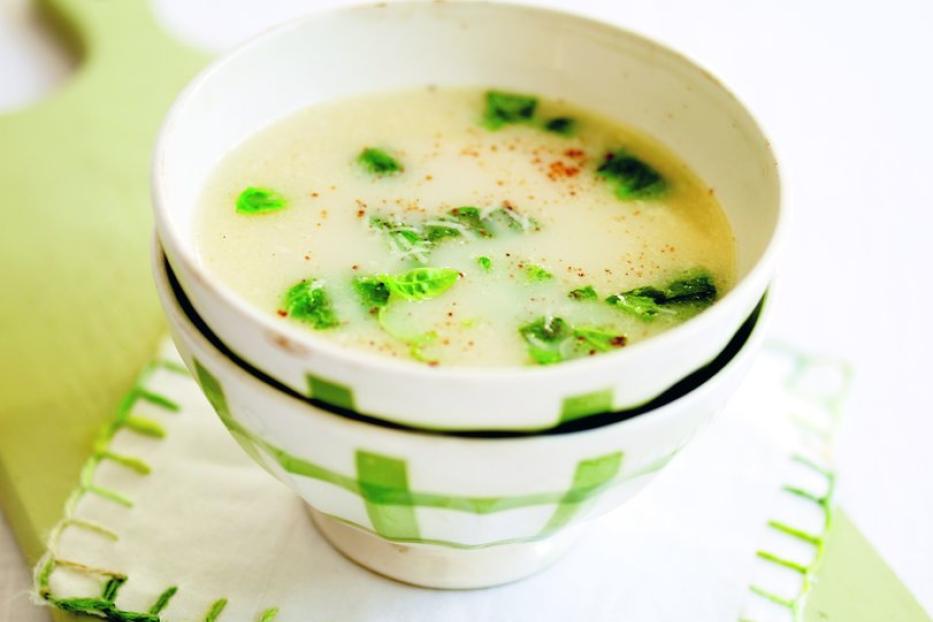 Eine Schüssel cremige Suppe mit grünen Kräutern auf einem grünen Schneidebrett.