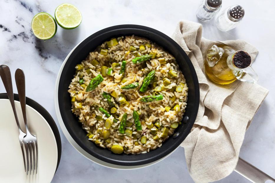 Risotto mit Spargel in einer Pfanne auf einem weißen Marmortisch. von oben aufgenommen. vegane und vegetarische gesunde italienische Küche.