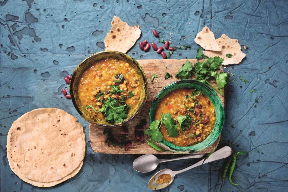 Zwei Schalen Linsensuppe mit Koriander und Brot auf einem Tisch.