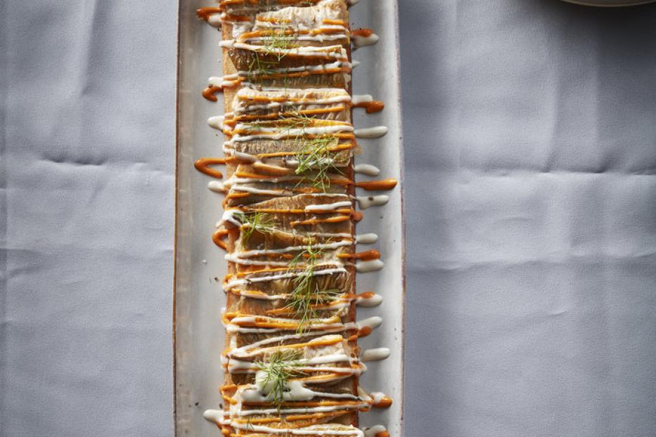 Ein längliches Gericht mit aufgereihten, belegten Brotscheiben, garniert mit Soße und Dill.