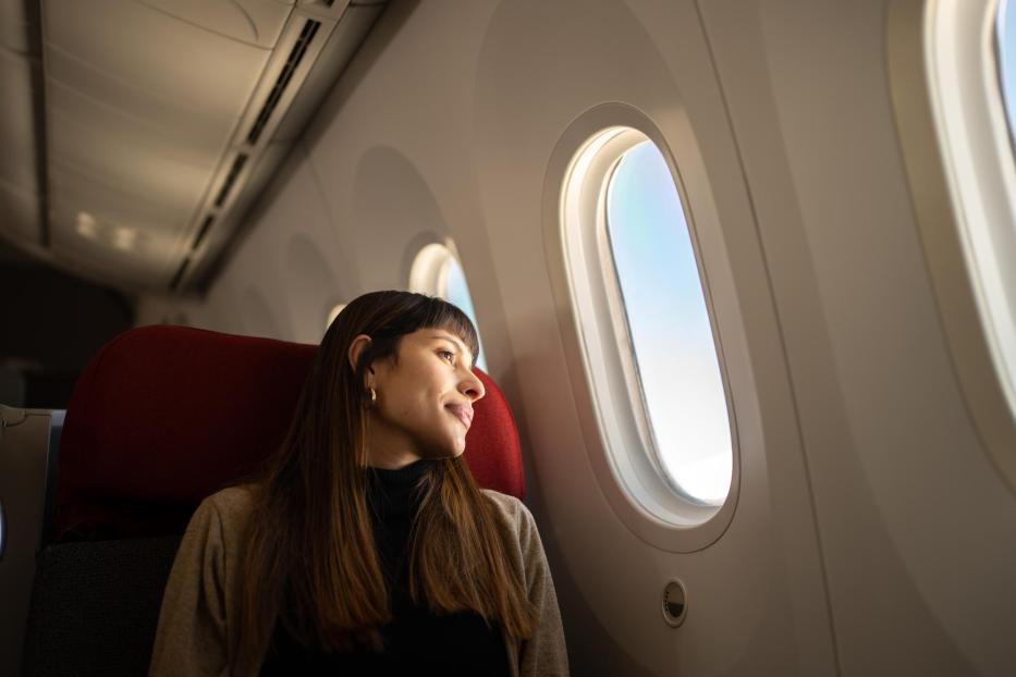 Junge Frau, die mit dem Flugzeug reist und aus dem Fenster schaut - Stock-Fotografie