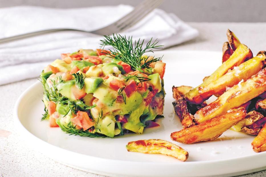 Ein Avocado-Tatar mit Tomaten und Dill wird mit Pommes Frites serviert.