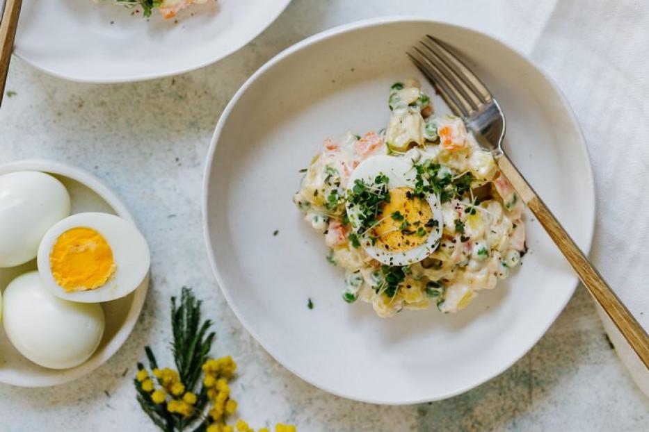 Zwei Teller mit russischem Salat, garniert mit einem halben Ei und frischen Kräutern.