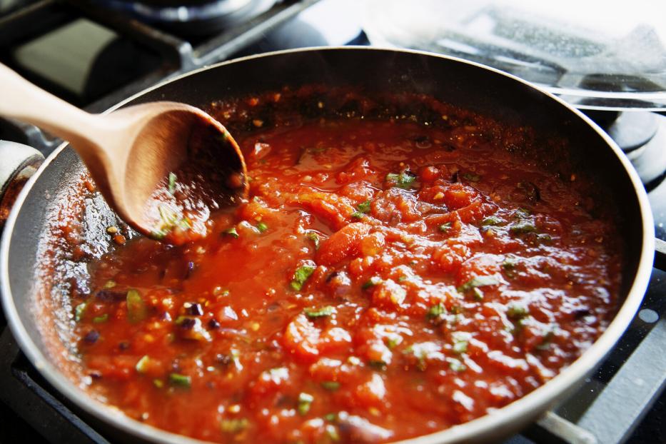 Eine Tomatensauce köchelt in einer Pfanne auf dem Herd.