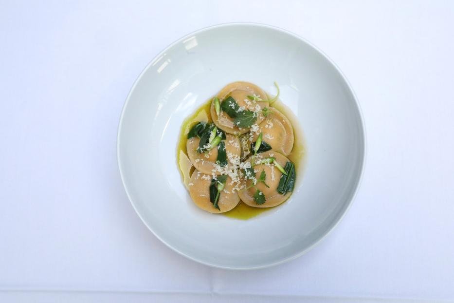 Ein Teller mit Ravioli, garniert mit Kräutern und geriebenem Käse.