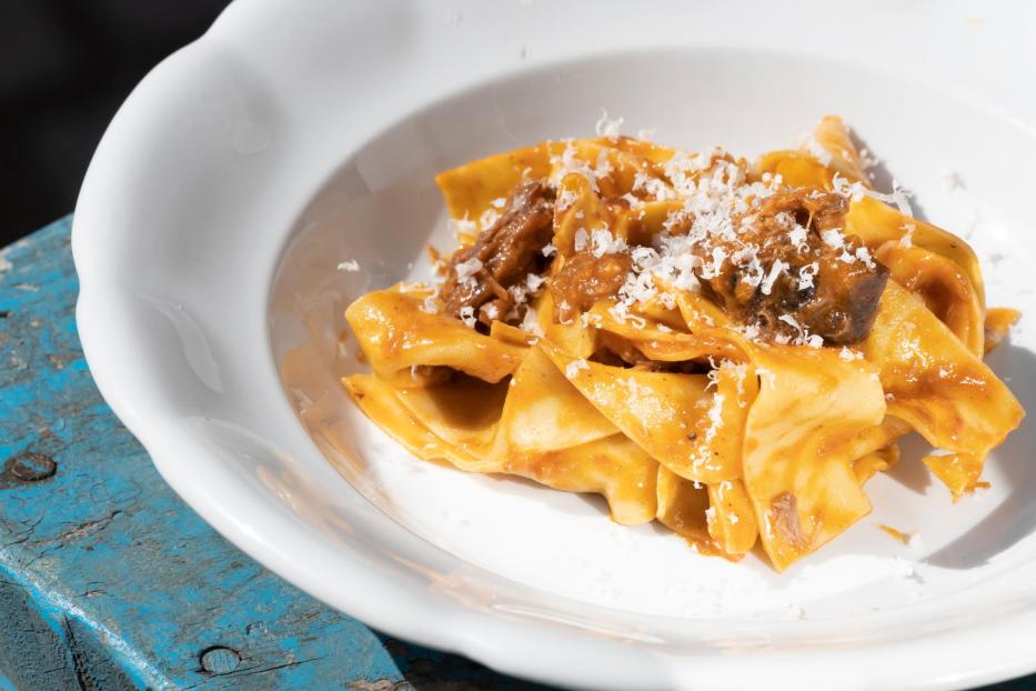 Ein Teller mit Bandnudeln und Fleischsoße, über die geriebener Käse gestreut wird.