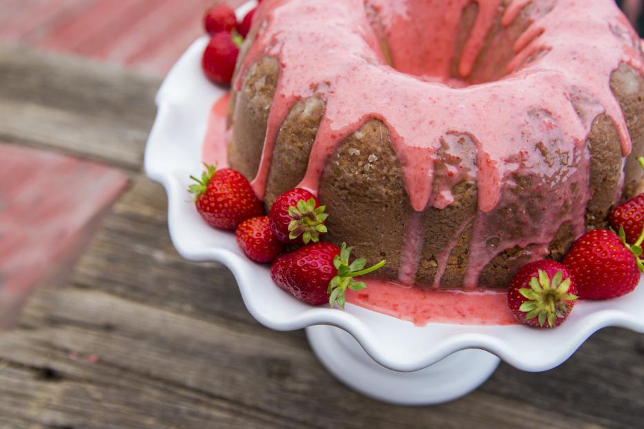 Ein Gugelhupf mit Erdbeerguss und frischen Erdbeeren auf einem weißen Teller.