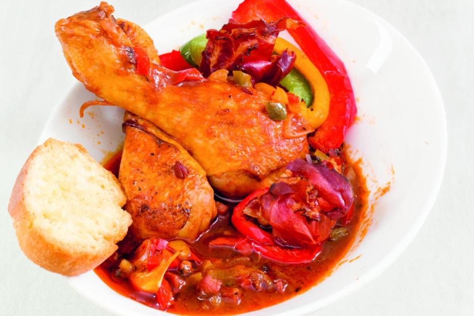 Hähnchenschenkel mit Paprika und Brot auf einem Teller angerichtet.