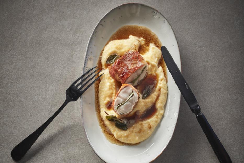 Auf einem Teller liegen Saltimbocca auf Polenta mit Salbei, dazu Messer und Gabel.
