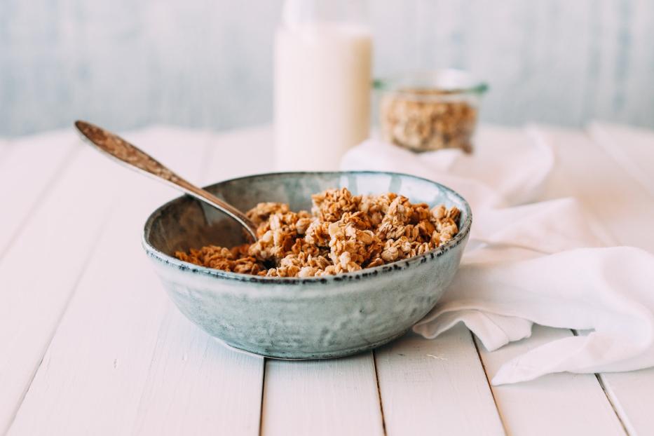 Eine Schüssel Müsli mit einem Löffel auf einem weißen Holztisch.