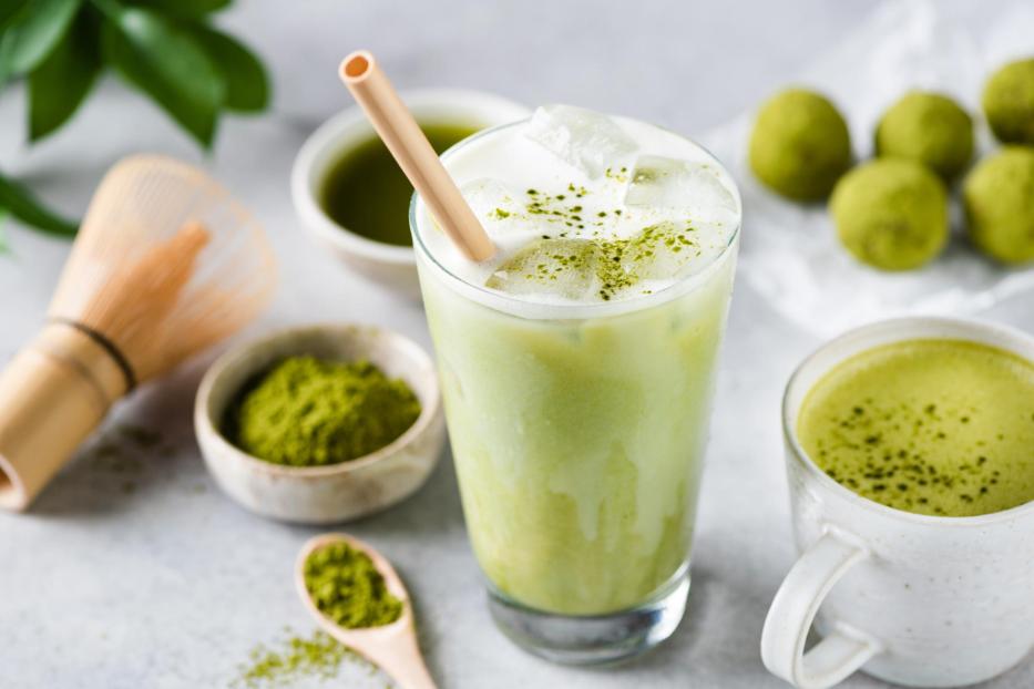 Ein Glas Matcha Latte mit Eis und ein Becher mit heißem Matcha-Tee stehen auf einem Tisch.