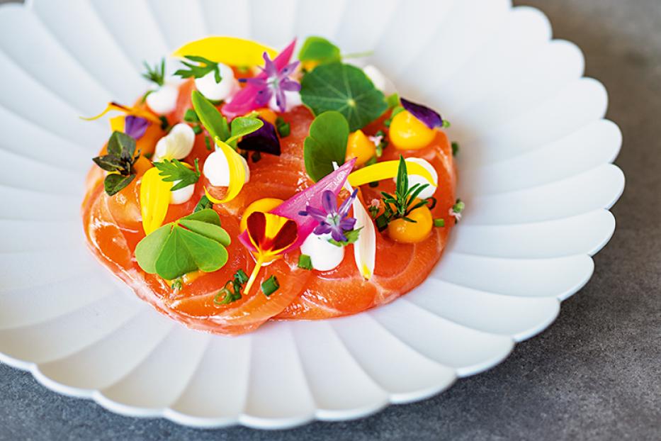 Ein Teller mit Lachscarpaccio, garniert mit Blüten und Kräutern.