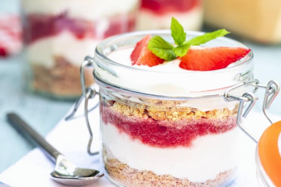 Ein Glas mit einem Dessert aus Erdbeeren, Joghurt und Keksstreuseln.