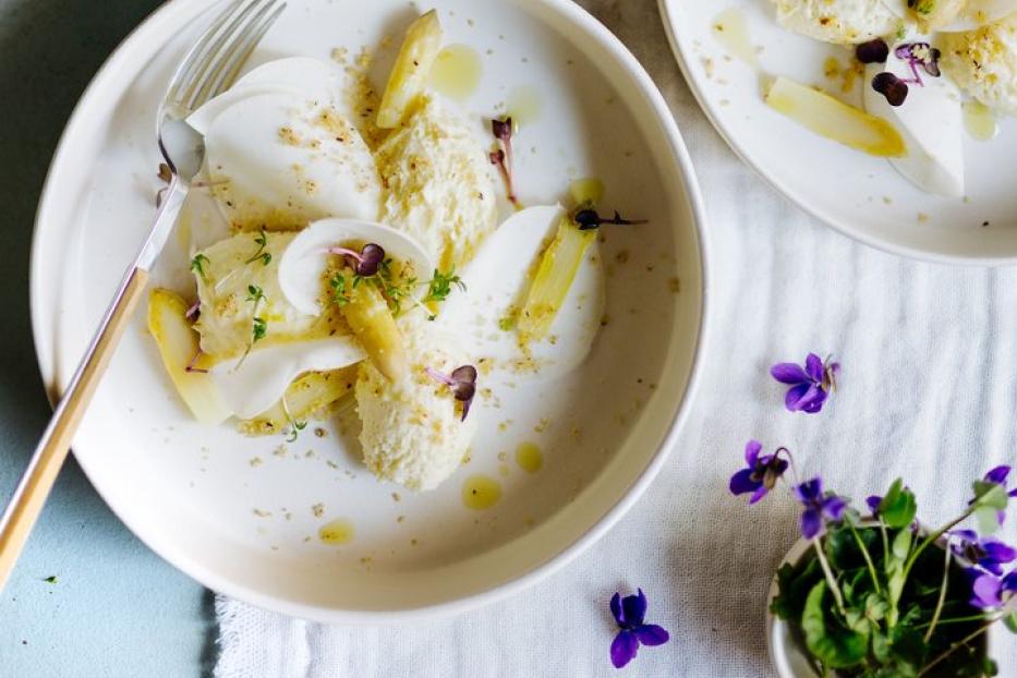 Zwei Teller mit Spargelsalat, garniert mit Veilchenblüten, auf einem Tisch.