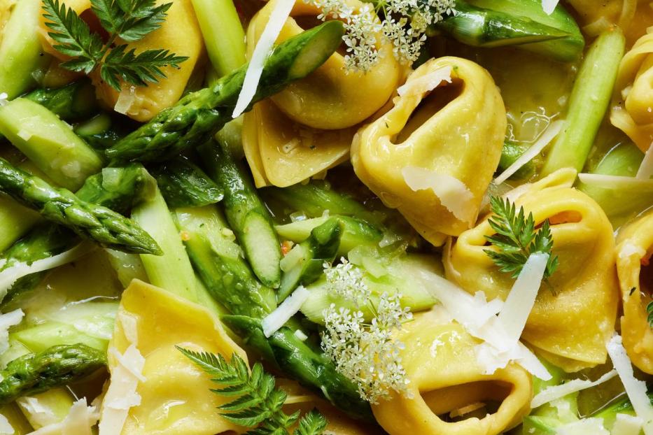 Eine Nahaufnahme von Tortelloni mit Spargel, Käse und kleinen weißen Blüten.
