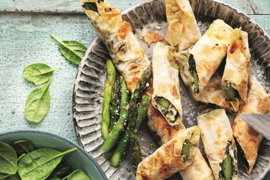 Eine Platte mit Filoteigröllchen, gefüllt mit Spargel und Spinat, dazu eine Schale mit frischem Spinat.