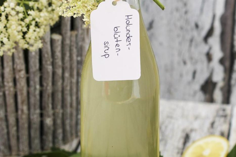 Eine Flasche Holunderblütensirup mit Zitronenscheiben und Minze auf einem Holztisch.
