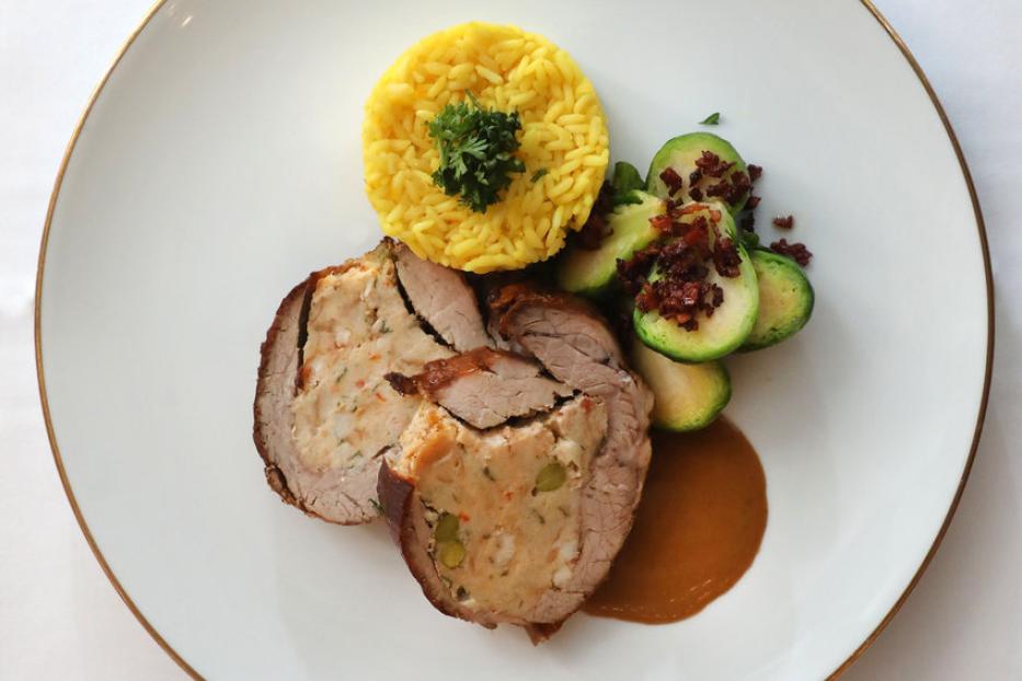 Ein Teller mit gefülltem Braten, gelbem Reis und Rosenkohl mit Speckwürfeln.