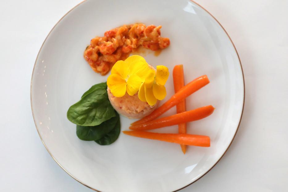 Ein Teller mit Krebsfleischsalat, garniert mit gelben Blüten, Babyspinat und Karotten.