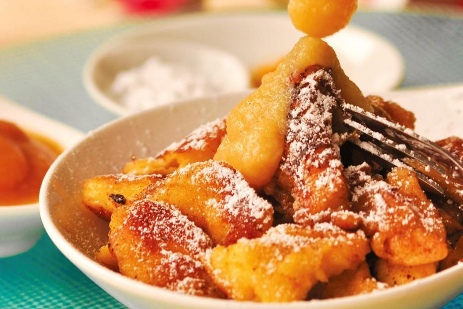 Grießschmarrn mit Apfelmus und Puderzucker in einer weißen Schale.