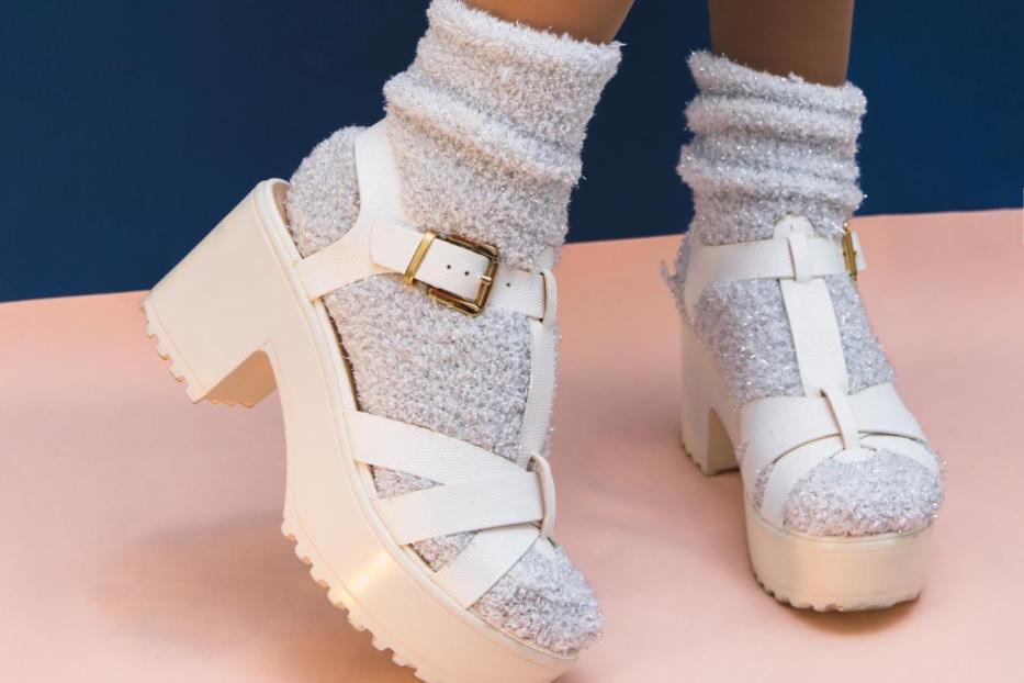 Beine in silbernen Socken und weißen Sommerschuhen vor pastellfarbenem, blau-rosa Hintergrund. Modekonzept.