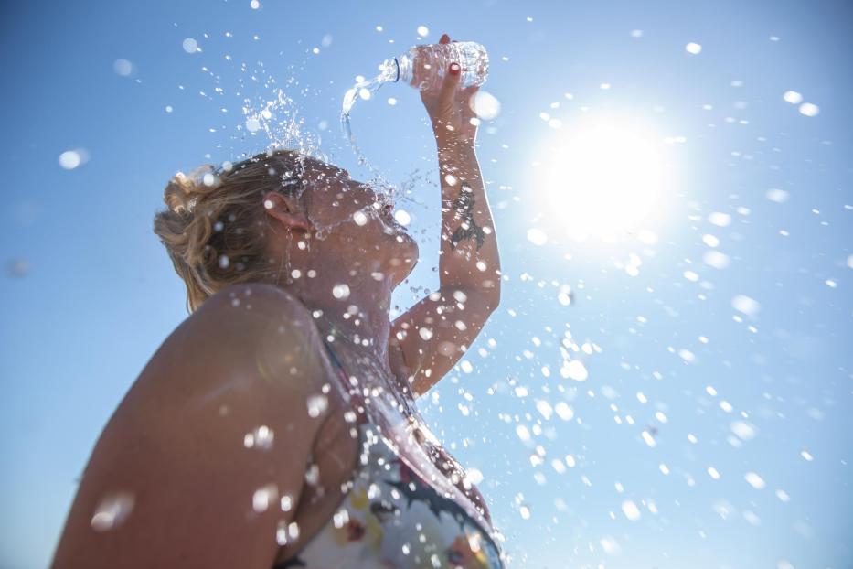 A young woman cools down with cold water during the summer heat. - Stock-Fotografie