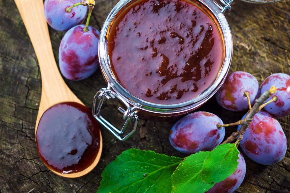 Ein Glas Pflaumenmus und frische Pflaumen auf einem Holztisch.