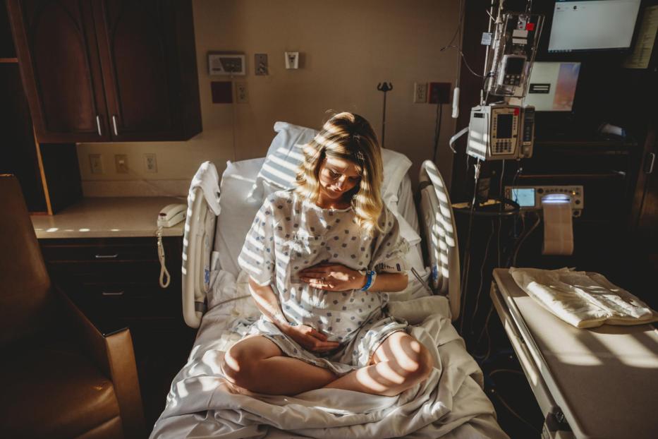 Pregnant woman touching stomach while sitting on bed in hospital - Stock-Fotografie