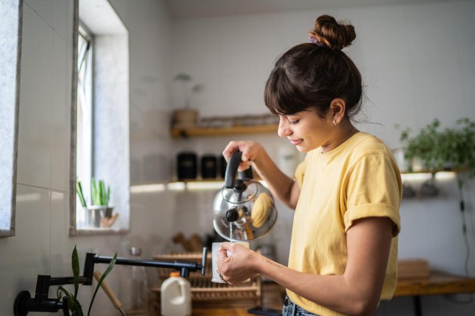 Junge Frau, die zu Hause einen Tee zubereitet - Stock-Fotografie