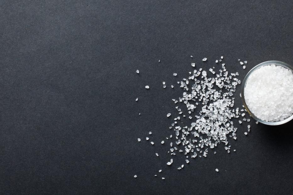 Ein Glas mit grobem Salz steht auf einer schwarzen Oberfläche.