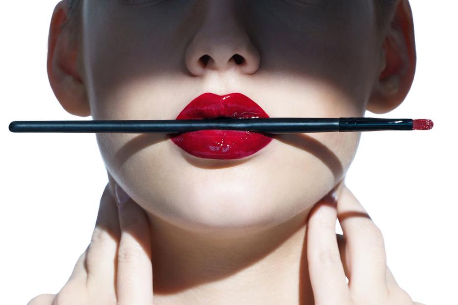 Eine Frau hält einen Lippenpinsel mit rotem Lippenstift zwischen ihren Lippen.