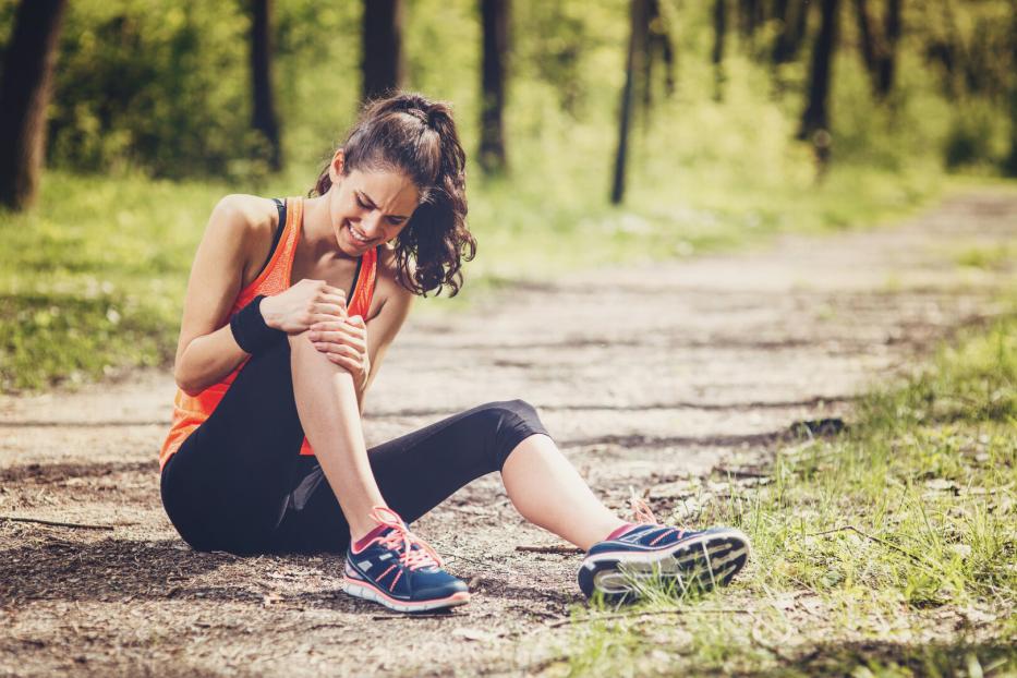 Frau beim Joggen hält sich das Knie, Schmerzen