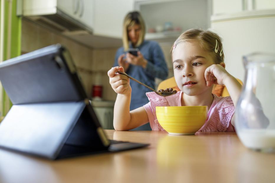 Mädchen schaut auf dem Tablet beim Frühstück essen