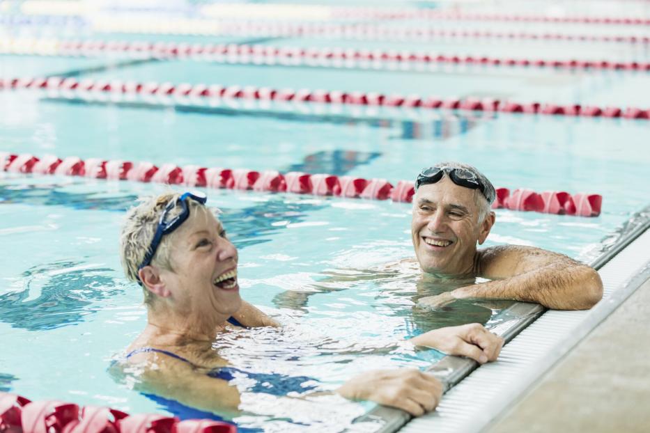 Ein älterer Mann und eine ältere Frau lehnen im Schwimmbecken am Rand.