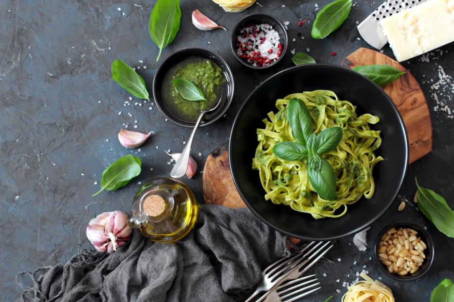 Pasta tagliatelle with pesto sauce and fresh basil leaves in black bowl.