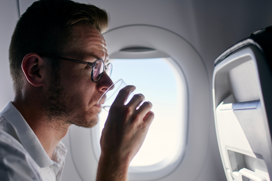 Mann sitzt im Flugzeug und trinkt Wasser