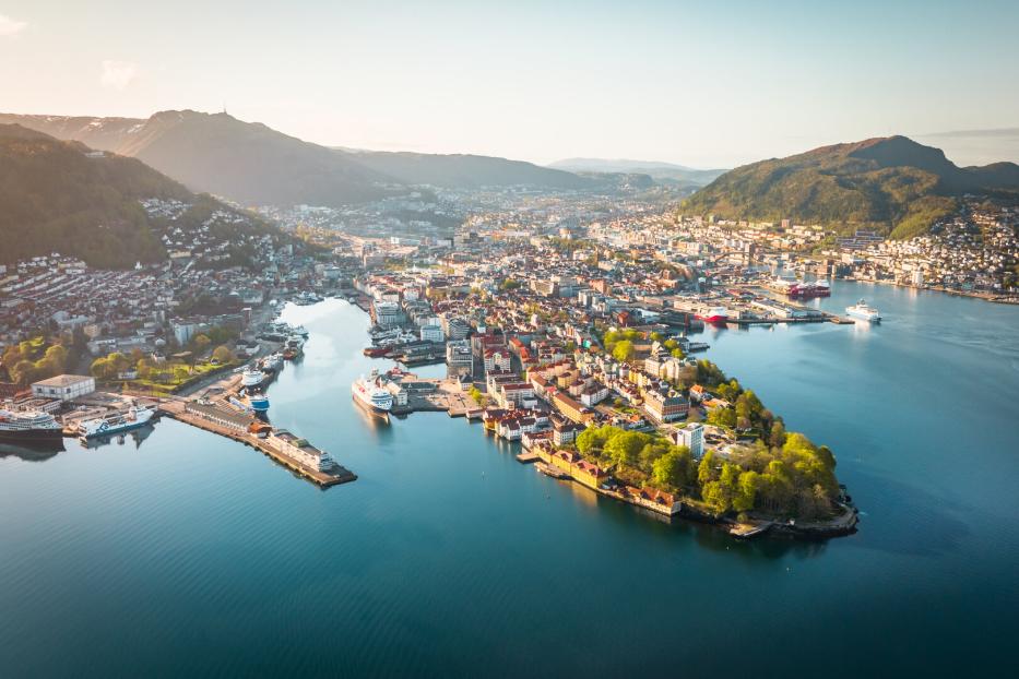 Blick auf Bergen mit der Bucht Vågen und dem historischen Stadtkern (links), den namensgebenden Hügeln und dem Hafen, an dem die bekannte Kreuzfahrtroute Hurtigruten beginnt (rechts)