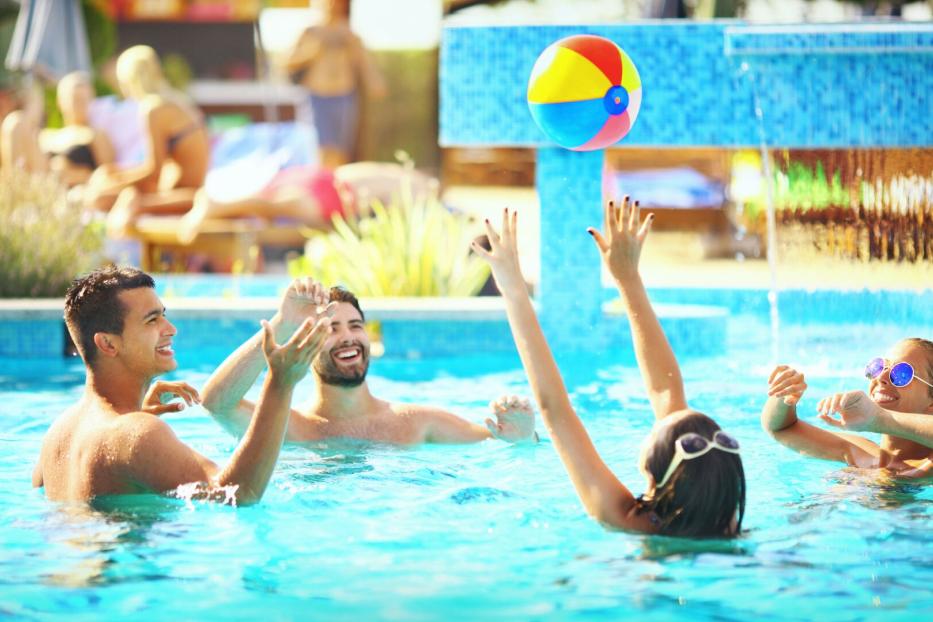 Freunde spielen Volleyball im Freibad.