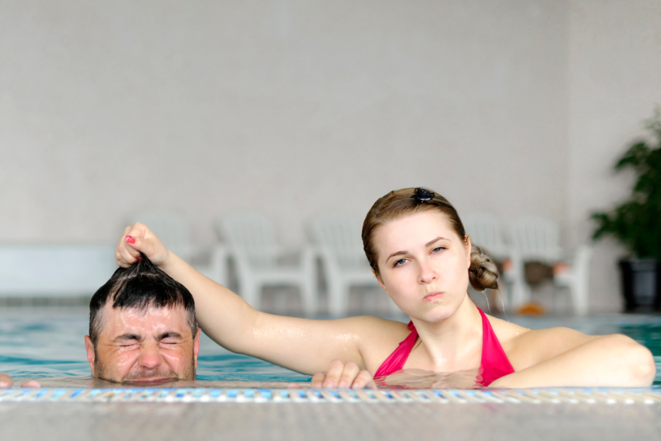 Frau und Mann im Pool, sie ist böse auf ihn und taucht ihn unter. Streit im Urlaub