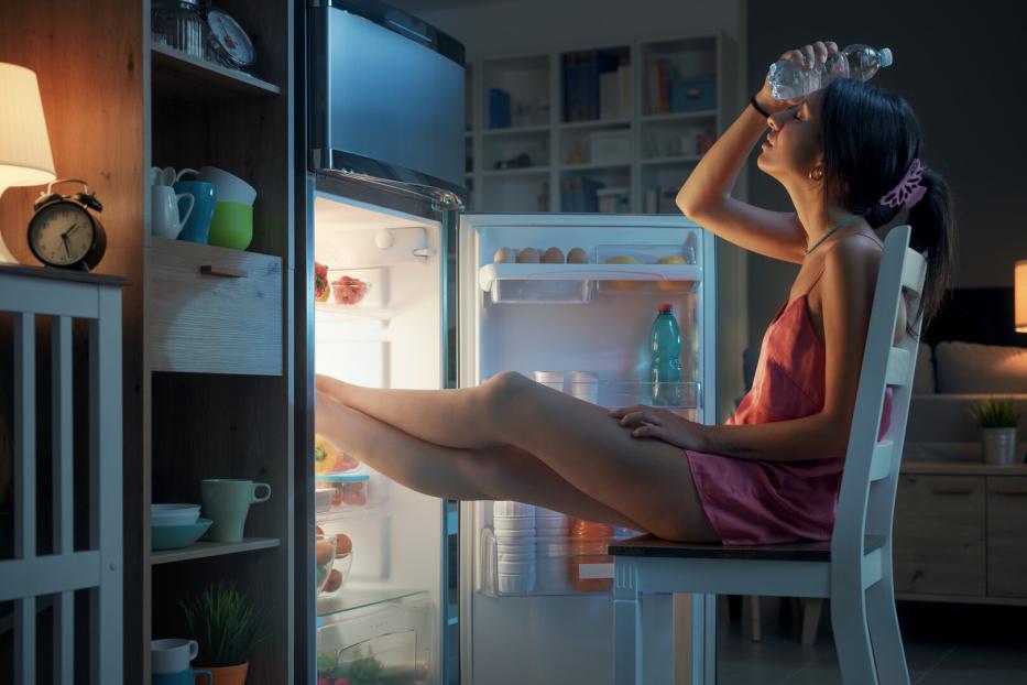 Eine Frau sitzt unter der Hitze leidend vor dem offenen Kühlschrank