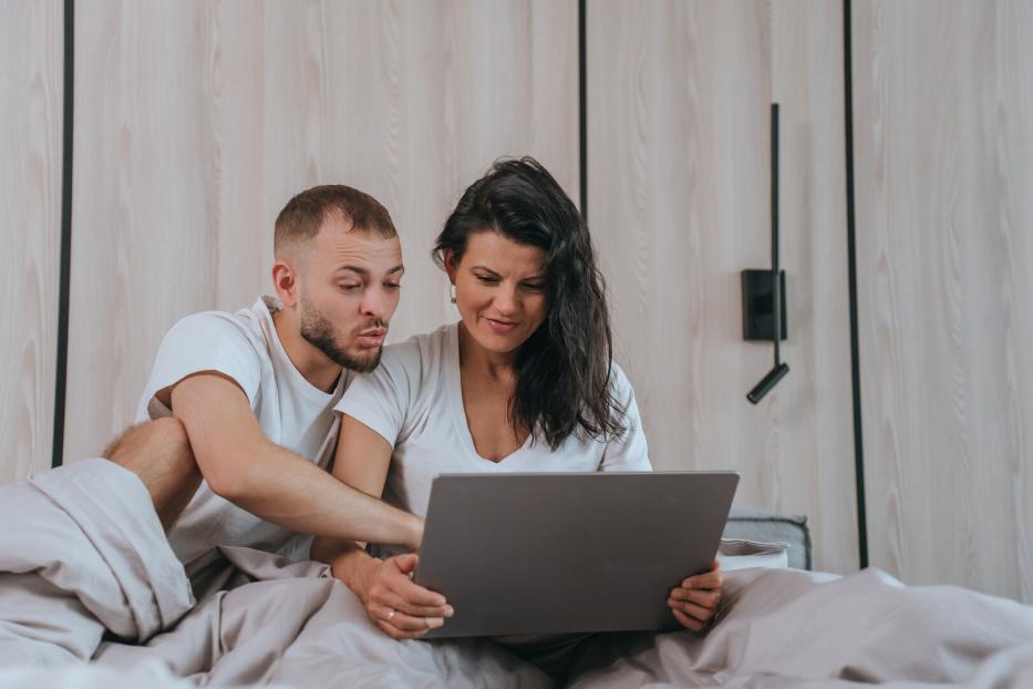 Ein Paar sitzt im Bett und schaut auf einen Laptop. 