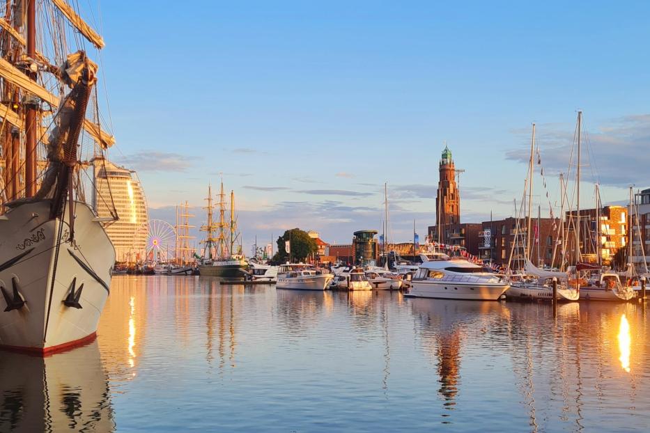 Ein Hafen voller Schiffe mit einem Riesenrad im Hintergrund im Sonnenuntergang.