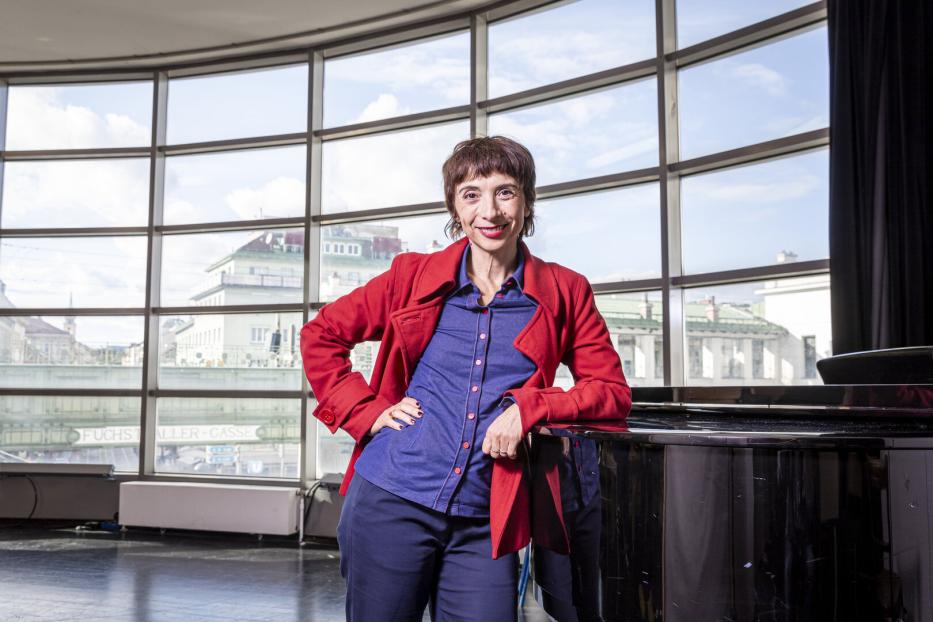 Ruth Brauer-Kvam steht an einem Klavier auf der Probenbühne der Wiener Volksoper. Der Raum hat ein großes Fenster. Im Hintergrund ist die Stadtbahn-Station Währiger Straße.