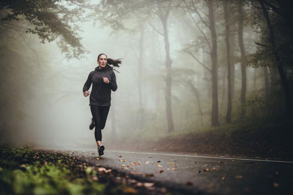 Junge Frau läuft im Wald bei nebligem Wetter. 