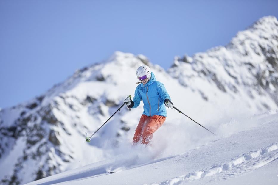 Skifahrerin wedelt über die Piste, der Schnee staubt