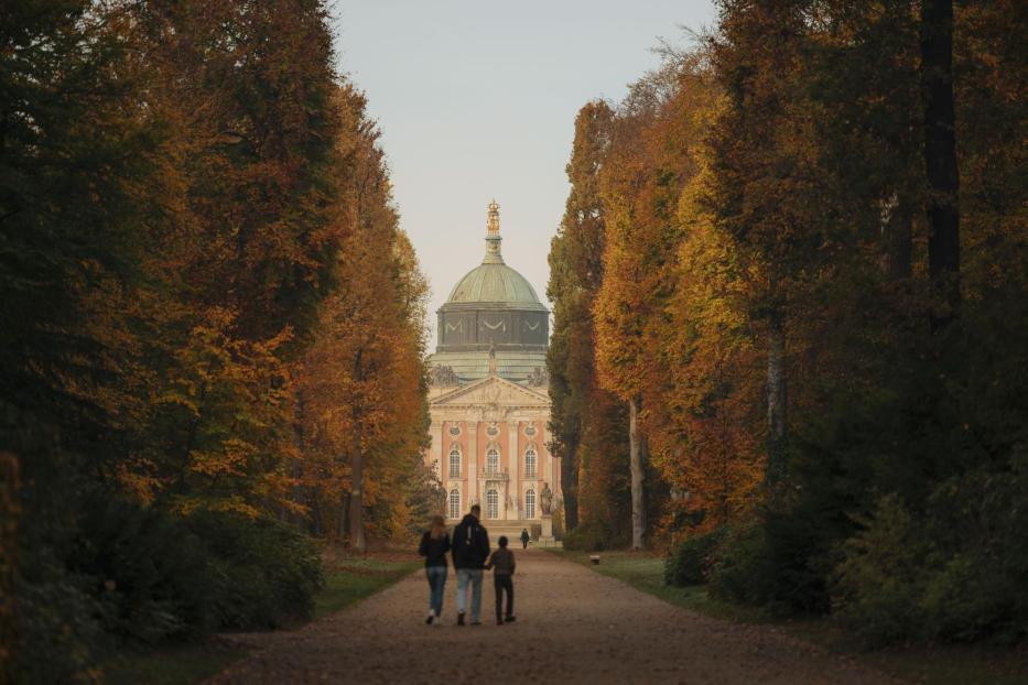 3. Ein Paar genießt einen Spaziergang mit ihrem Hund auf einem ruhigen Weg in der Natur. Am Ende des Weges steht ein Schloss.