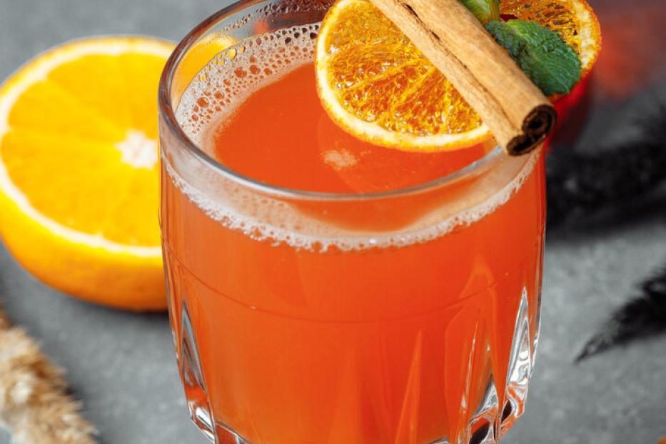 Ein Glas mit einem orangefarbenen Getränk, garniert mit Orange, Zimtstange und Minze.