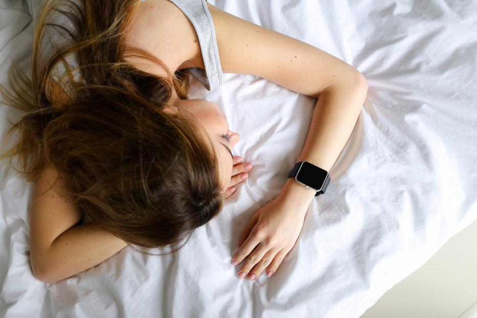 eine Frau liegt schlafend mit einer Smartwatch am Handgelenk im Bett