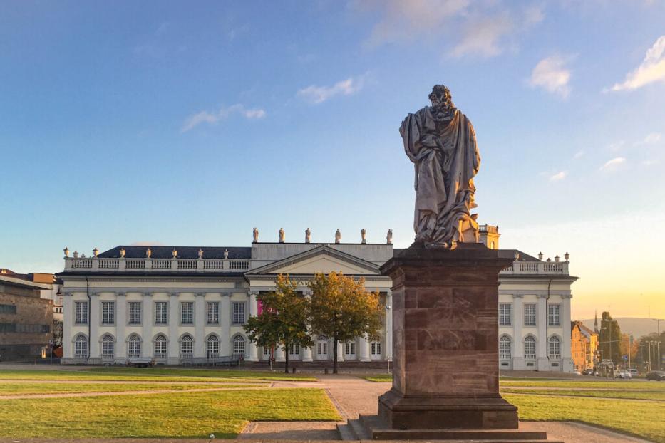 Statue eines Mannes vor einem Gebäude, das die architektonische Schönheit der Umgebung betont.